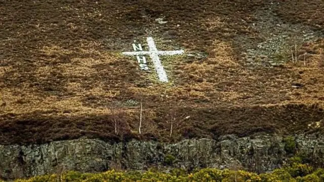 cross on hillside and letters NHS