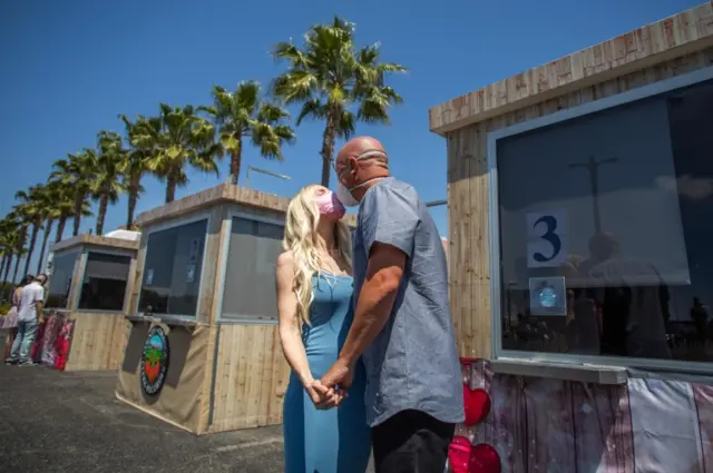 Chad Robbins and Tracey Robbins (R) kiss wearing face masks after their wedding ceremony officiated by a clerk recorder at the Honda Center parking lot