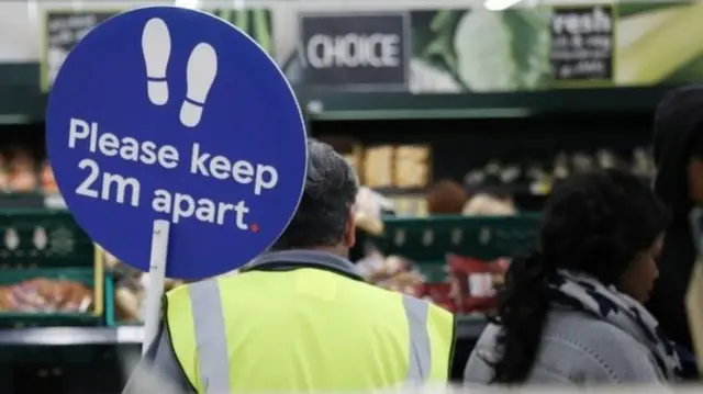 Supermarket with worker holding social distancing sign