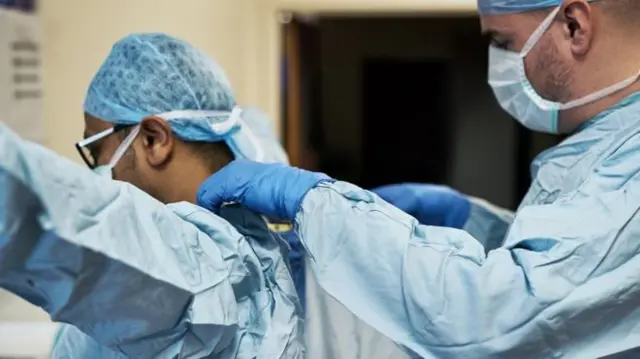 Doctors helping each other wear their PPE