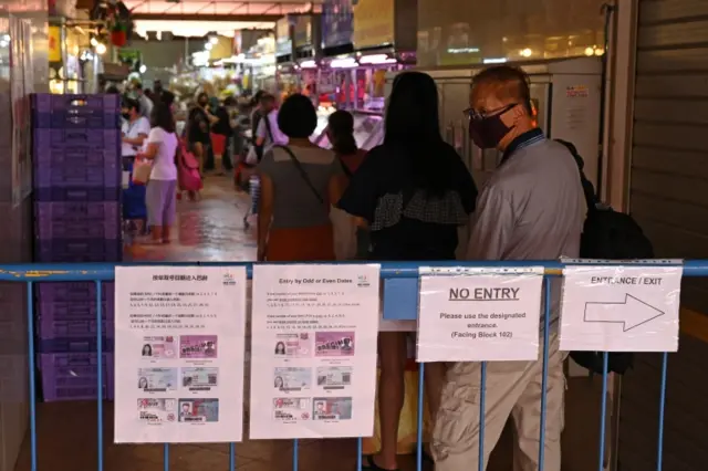 Instruction notice placards hang on a barrier as a man wearing a facemask as a prevention measure against the spread of the COVID-19 coronavirus queues to enter a wet market in Singapore