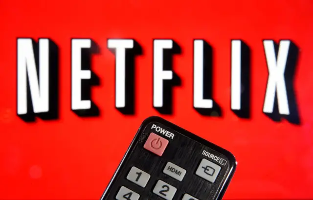 In this photo illustration, a remote control is seen in front of a television screen showing a Netflix logo