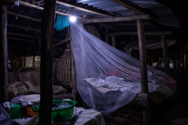 A trader sleeps wrapped in a mosquito net to protect from malaria