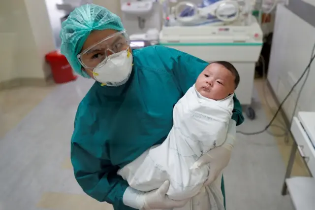 A nurse poses for a picture with a one-month-old Thai baby