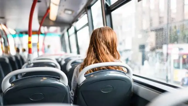 A stock image of a woman sitting alone on a bus