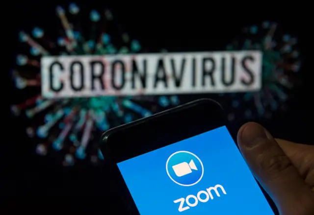 Zoom logo seen displayed on a smartphone with a computer model of the COVID-19 coronavirus on the background.