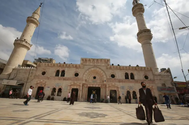 A man carrying his shopping bags walks ijn front of a mosque, ahead of the Muslim holy month of Ramadan, during the novel coronavirus pandemic crisis in the Jordanian capital Amman, on April 23, 2020.