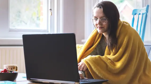 Woman home-working with a blanket over her shoulders