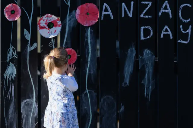 Three-year-old Louise Boivin places a poppy onto the fence of her family home on April 25, 2020 in Christchurch, New Zealand