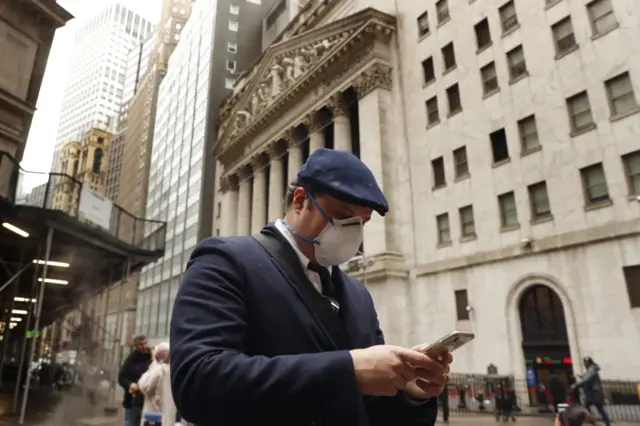 A man wearing a mask walks past the New York Stock Exchange