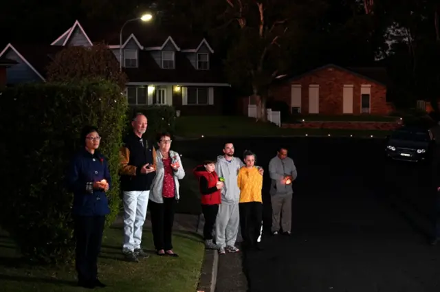 People stand outside their house in Sydney holding candles