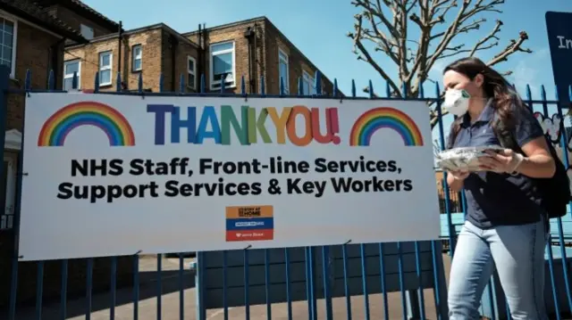 Woman walks past a sign thanking NHS staff in London