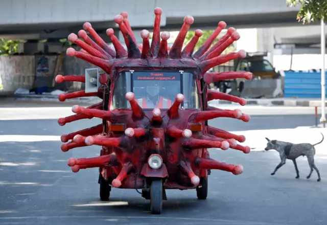 A man riding a tuk tuk decorated to look like coronavirus