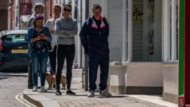 Shoppers queue outside a shop