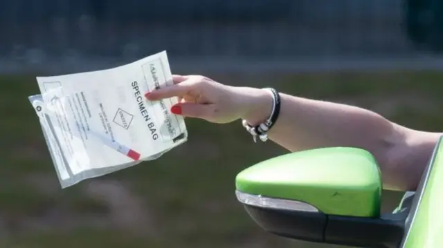 A wman handing in test results at a drive-in centre