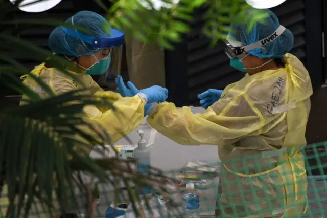 Healthcare workers dressed in personal protective equipment prepare to collect nasal swab samples from migrant workers