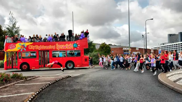 Dancers follow a sightseeing bus in Ipswich