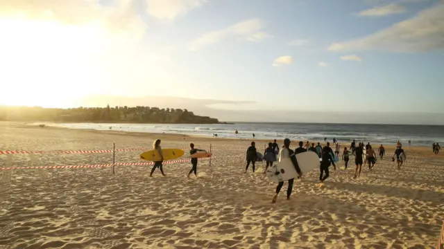 Surfers walk down Bondi Beach towards the water on the first day of the beach re-opening