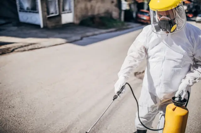 A man in a disinfectant suit spraying on the street