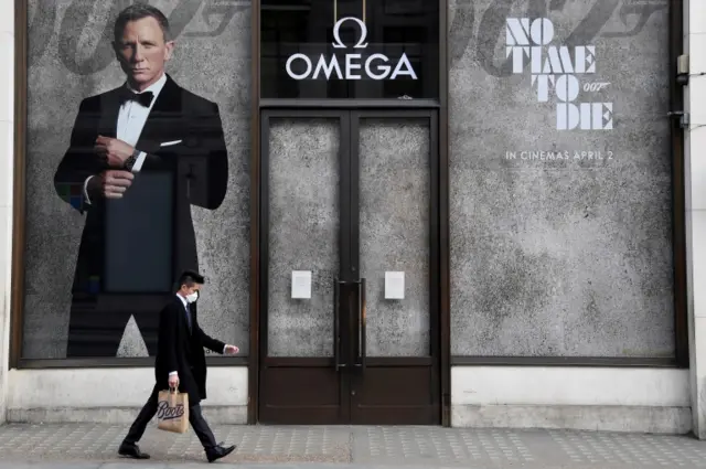 A man wearing a protective face mask walks past a shop promoting a new James Bond movie "No Time To Die",