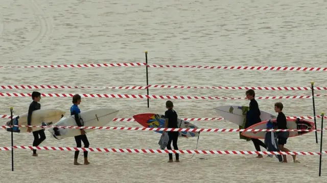 Boys carry surfboards in a taped-off path across Bondi Beach