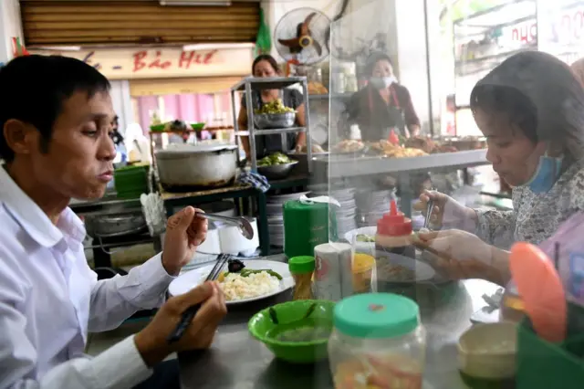 People eat their meal on a table installed with a make-shift plastic partition, Hanoi