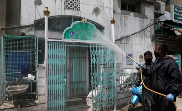 A worker sprays a mosque with disinfectant