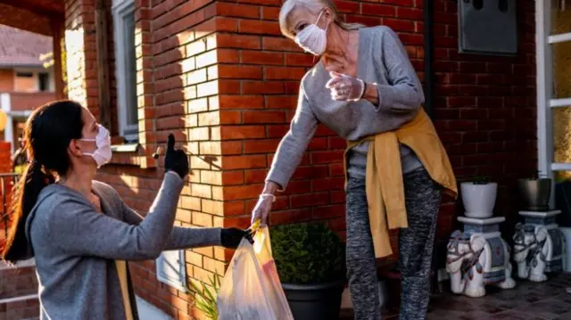 A woman wearing a face mask collects a delivery on her doorstep