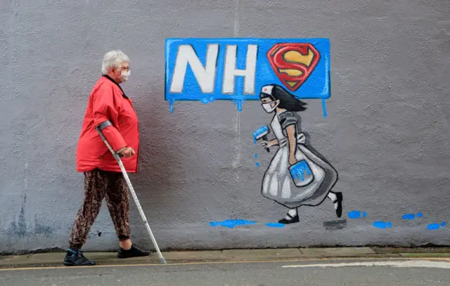 A woman wearing a facemask walks past a mural on the side of Horse Vaults pub in Pontefract, Yorkshire