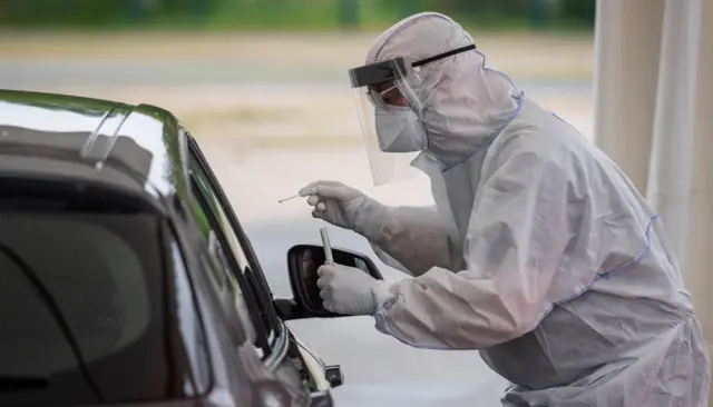 A doctor wearing protective gear, face shield and face mask gathers a saliva sample in Berlin on 30 April