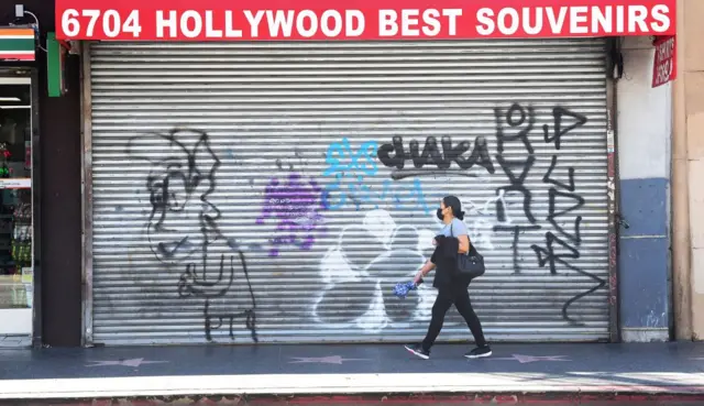 A masked pedestrian walks past shuttered shopfronts in Hollywood, California