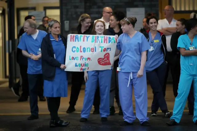 30/04/2020 Reuters NHS workers are seen with a birthday poster for Captain Tom Moore outside the Aintree University Hospital during the Clap for our Carers campaign in support of the NHS, following the outbreak of the coronavirus disease