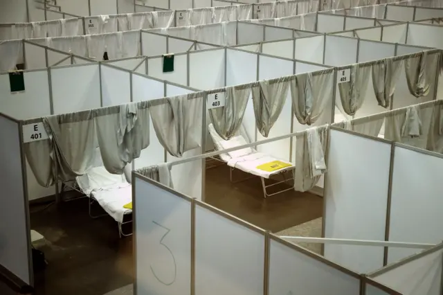 Hospital beds are separated by dividing walls and curtains