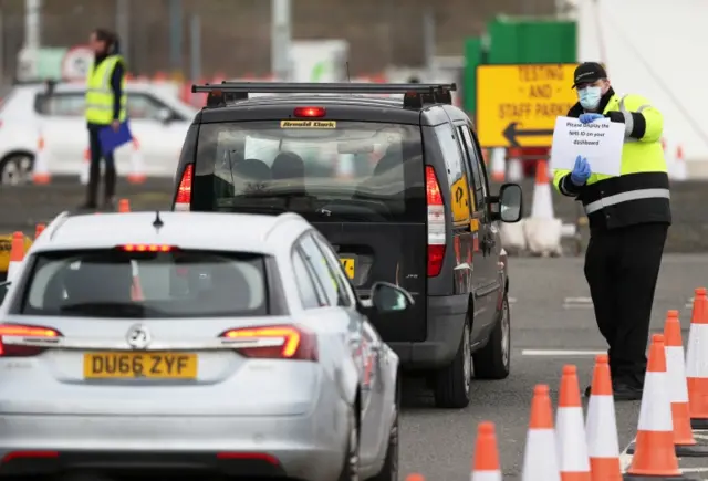 A worker holds up a sign for NHS staff driving into the testing facility at Glasgow Airport