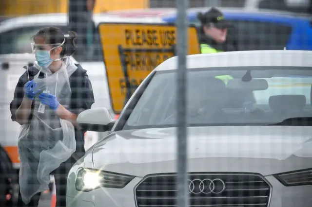 A medical worker waits by a car to test NHS staff at Glasgow Airport