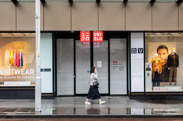 A woman wearing a face mask walks past the closed Uniqlo store in the central business district following the temporary closure of Uniqlo stores in Melbourne, Australia (April 05, 2020).