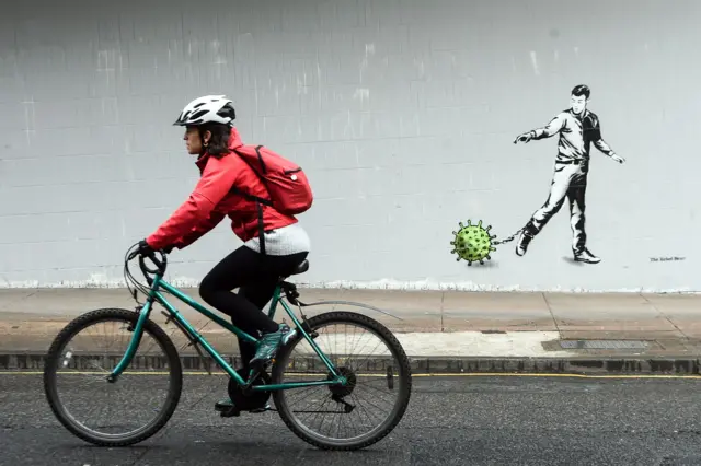 A cyclist passes a Coronavirus-inspired piece of graffiti in Glasgow