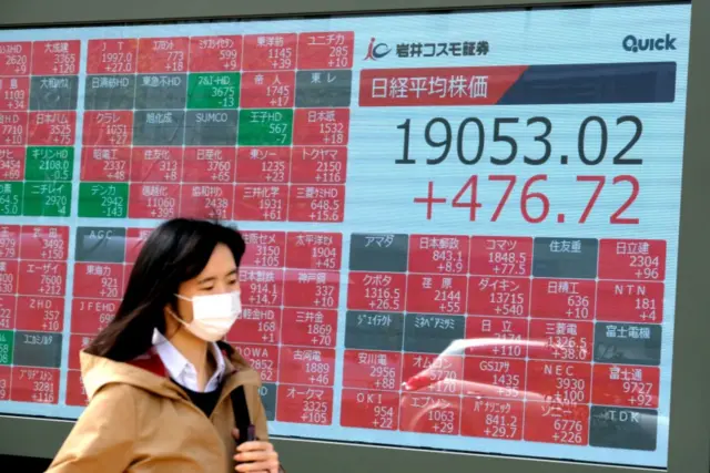 A pedestrian walks past a quotation board displaying share prices of the Tokyo Stock Exchange in Tokyo (7 April 7 2020).