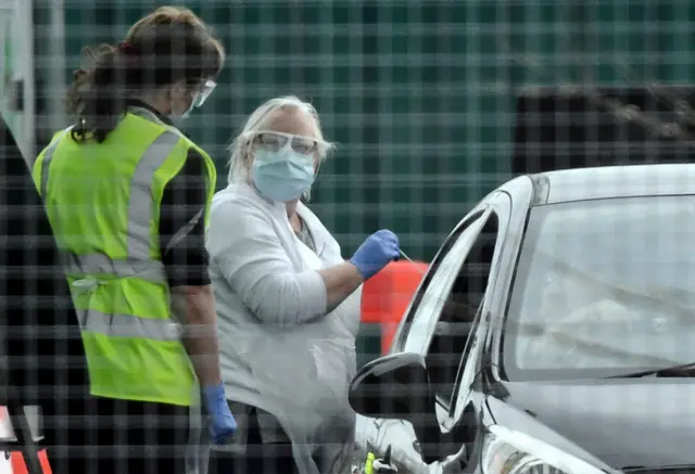 A medical staff member wearing gloves, eye protection and a face mask, tests an NHS worker at a drive-in facility set up in the car park of Glasgow Airport