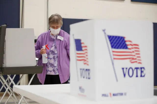 An observer cleans a voting booth at a school gym in Kenosha