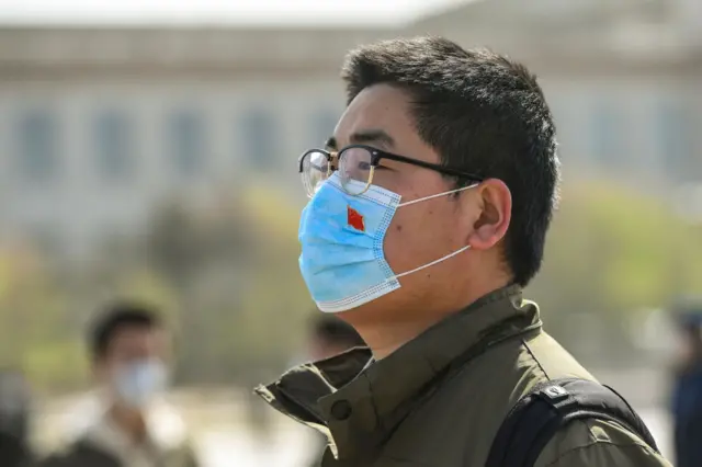 A man stands in silent tribute with a protective mask