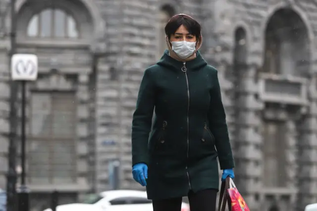 A woman wearing a face mask and gloves as a precaution against the spread of coronavirus walks along the subway