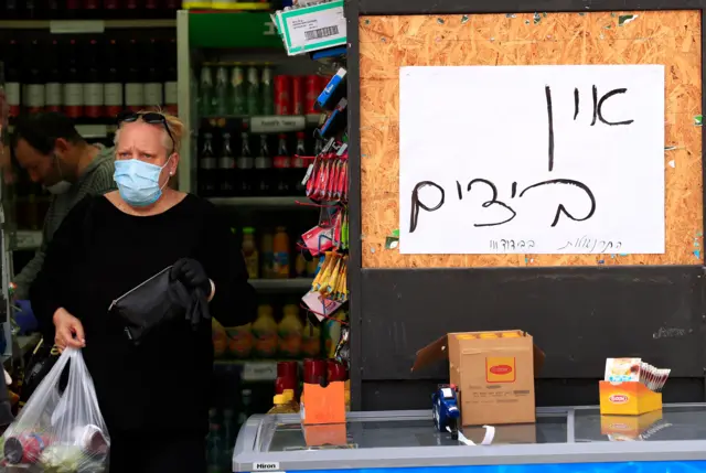 A shopper wearing a face mask walks past a sign saying “no eggs” at a market in Jerusalem (6 April 2020)