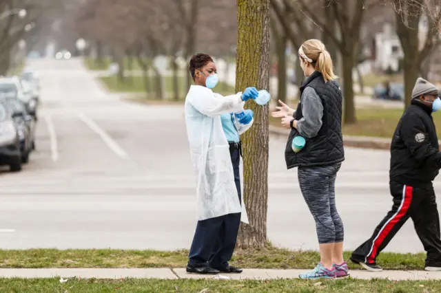 A woman hands out surgical masks to people standing in line to vote in Wisconsins spring primary election on 7, April, 2020