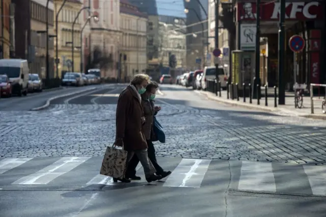 Two elderly women cross a street in Prague wearing face masks