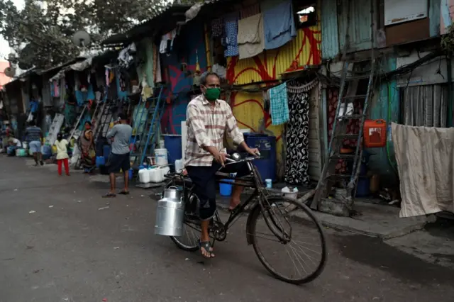 A milkman wearing a mask rides a bike in Dharavi slum, Mumbai