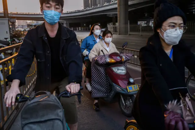 Chinese commuters wear protective masks as they wait to cross a road in the central business district on April 7, 2020 in Beijing