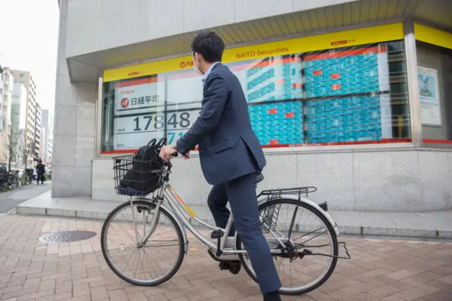 A man rides a bicycle past an electronic share quote board in Tokyo