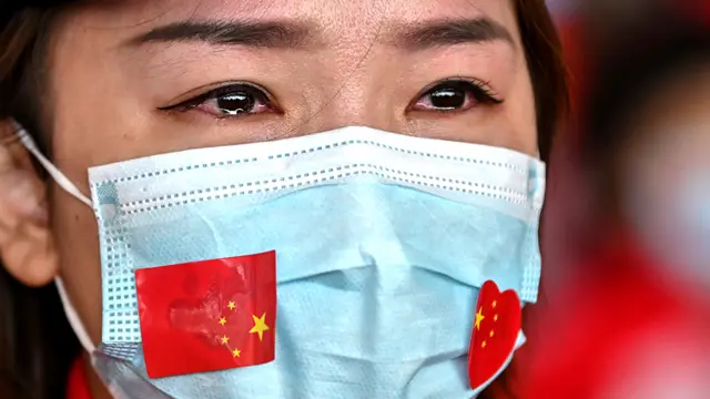 A female medical worker wearing a face mask with Chinese flags attached to it cries at a ceremony at Wuhan's Tianhe Airport