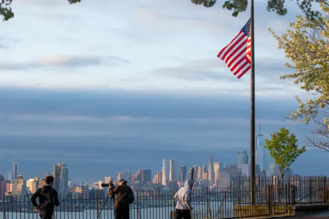 Flags are flying at half-mast as the sun rises behind Manhattan on 6 April, 2020